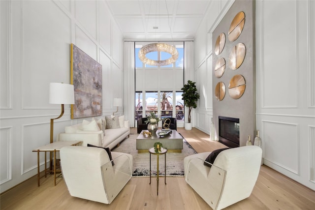 living room featuring a glass covered fireplace, a decorative wall, light wood-style flooring, and a high ceiling