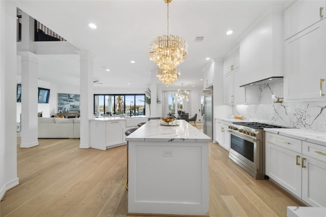 kitchen with high end appliances, light wood-style floors, white cabinetry, a chandelier, and a center island