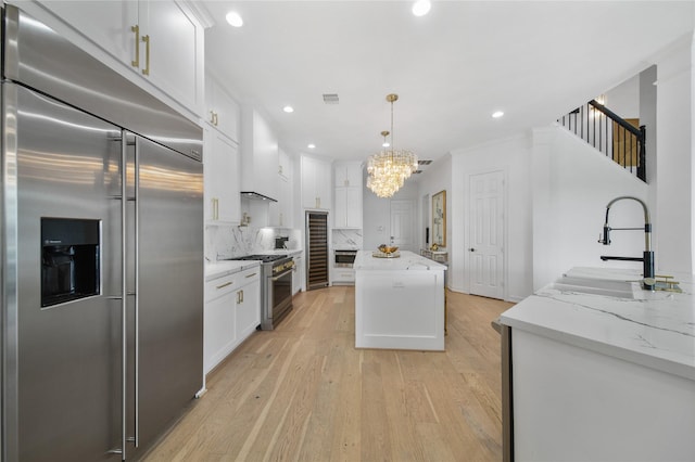 kitchen featuring high end appliances, light wood finished floors, a sink, decorative backsplash, and wall chimney range hood