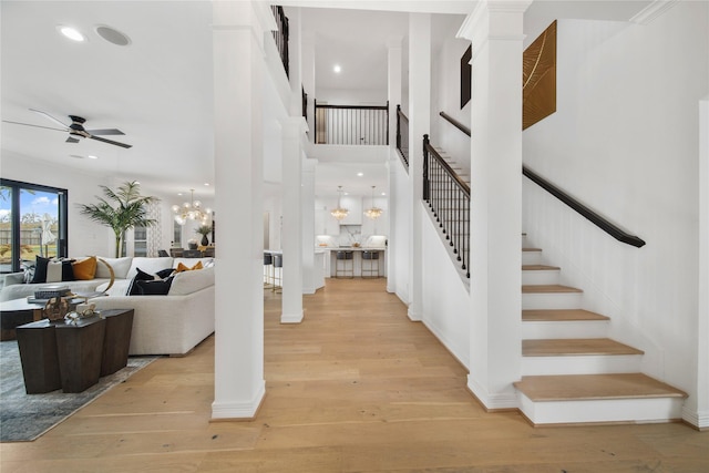 entryway featuring light wood-style flooring, ceiling fan with notable chandelier, recessed lighting, stairway, and ornate columns