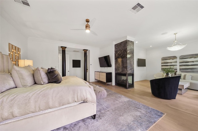 bedroom with a tiled fireplace, visible vents, crown molding, and wood finished floors