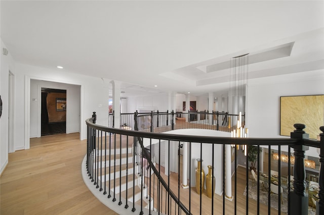 hallway with an upstairs landing, a tray ceiling, recessed lighting, light wood-style floors, and decorative columns