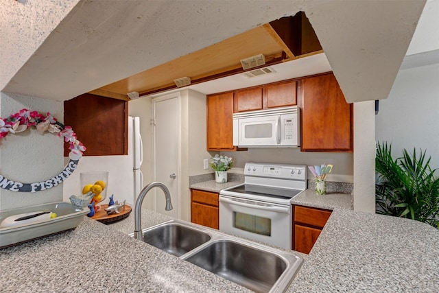 kitchen featuring visible vents, brown cabinets, a sink, white appliances, and light countertops