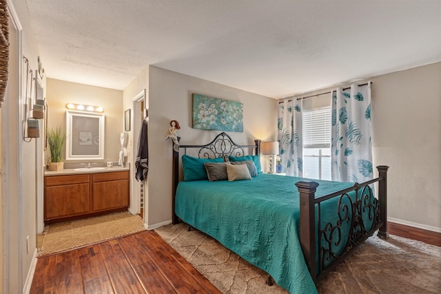 bedroom with ensuite bath, wood finished floors, baseboards, and a sink