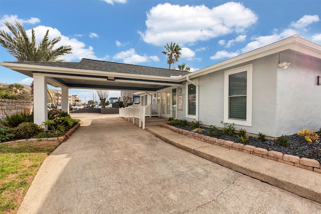 exterior space with concrete driveway, roof with shingles, and stucco siding