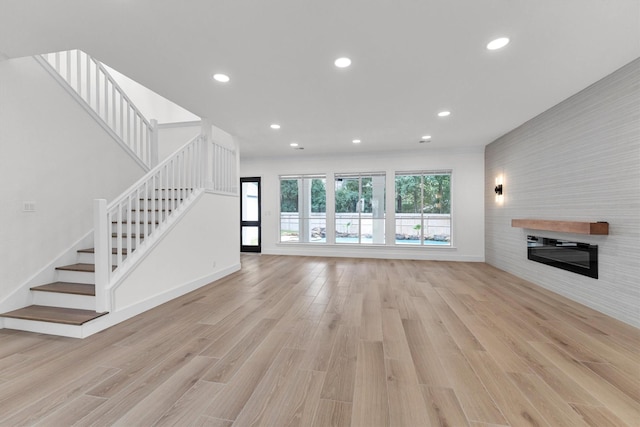 unfurnished living room featuring a glass covered fireplace, stairway, recessed lighting, and light wood finished floors