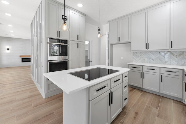 kitchen with double oven, light wood-style flooring, black electric cooktop, and light countertops