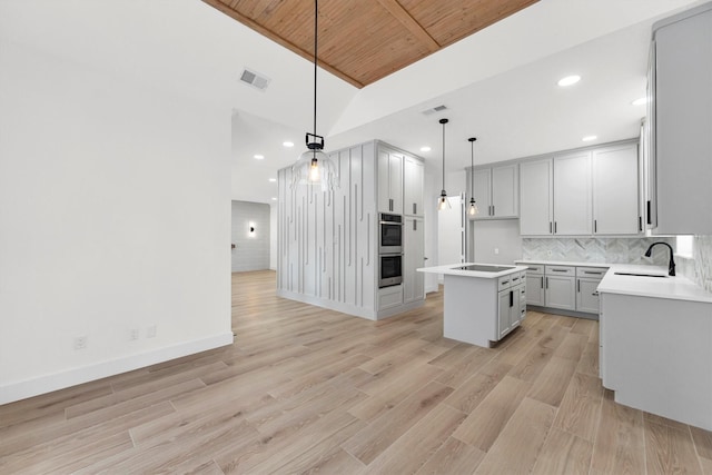 kitchen with visible vents, light wood-style flooring, a sink, a kitchen island, and decorative backsplash