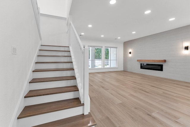 stairs featuring a glass covered fireplace, recessed lighting, and wood finished floors