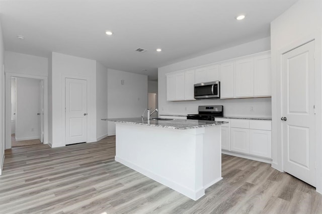 kitchen featuring visible vents, light wood finished floors, an island with sink, a sink, and stainless steel appliances