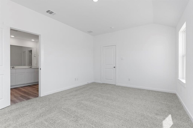 carpeted spare room with visible vents, baseboards, and vaulted ceiling