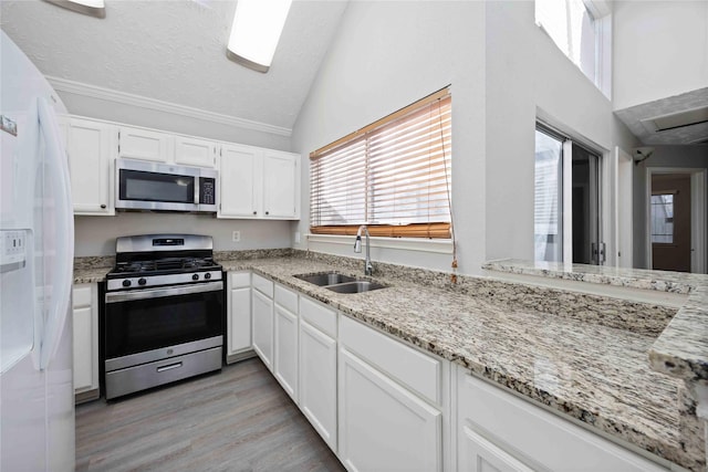 kitchen with vaulted ceiling, stainless steel appliances, a textured ceiling, white cabinetry, and a sink