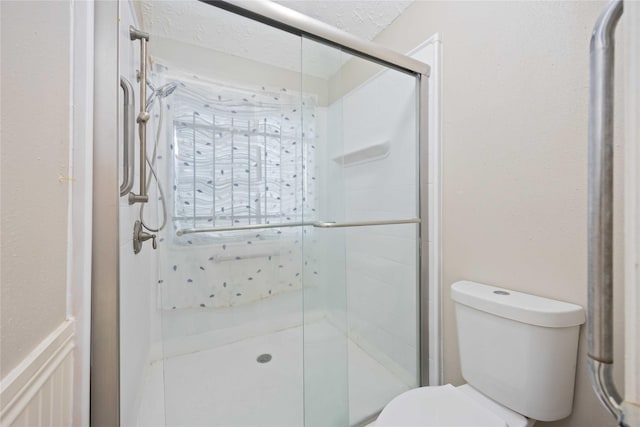 bathroom featuring toilet, a stall shower, and a textured ceiling