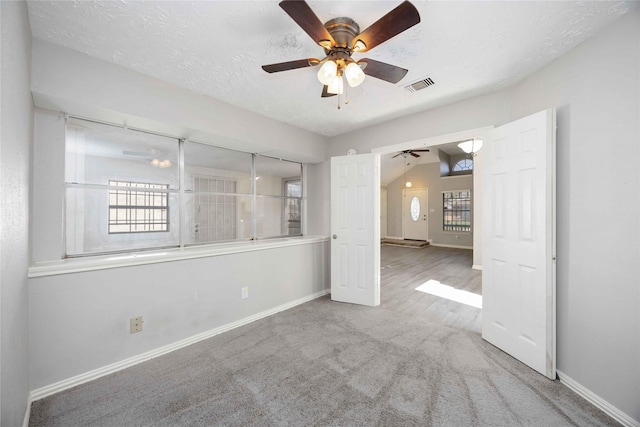 carpeted spare room featuring a textured ceiling, a healthy amount of sunlight, visible vents, and ceiling fan