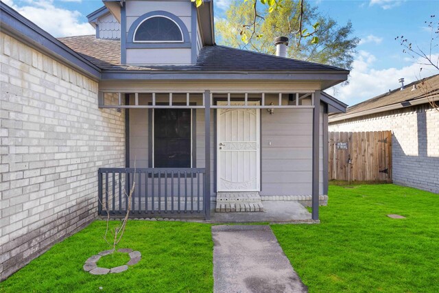 property entrance with a lawn, a shingled roof, and fence