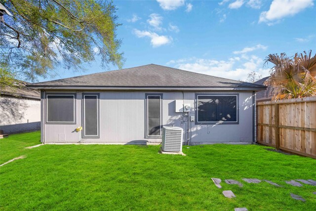 rear view of house featuring central air condition unit, a lawn, roof with shingles, and fence