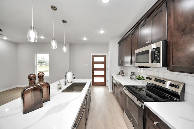 kitchen with dark brown cabinetry, decorative backsplash, light wood-style floors, stainless steel appliances, and a sink