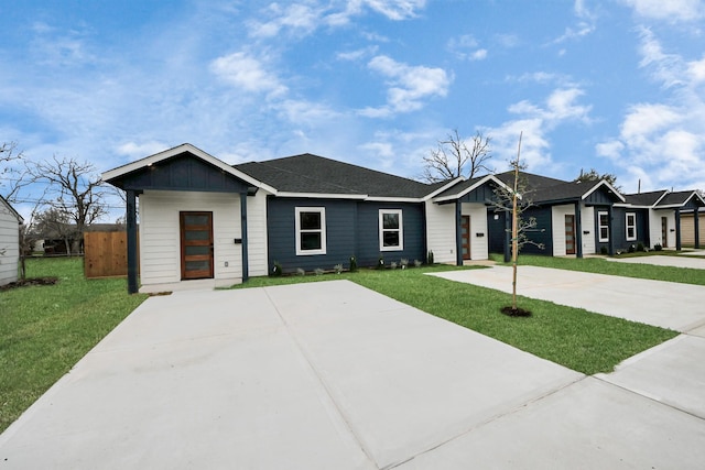 view of front facade featuring board and batten siding, a front lawn, fence, roof with shingles, and driveway