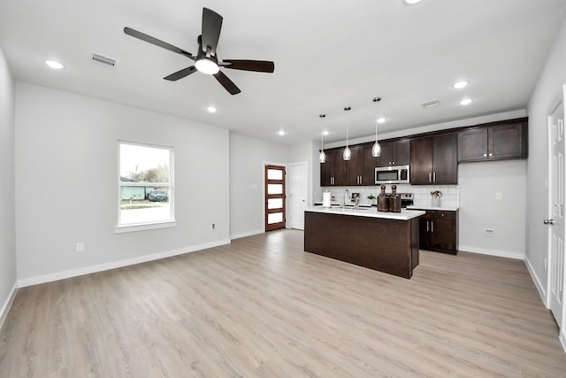 kitchen with stainless steel microwave, light wood finished floors, decorative backsplash, dark brown cabinets, and light countertops