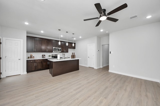 kitchen with visible vents, a center island with sink, appliances with stainless steel finishes, light countertops, and dark brown cabinets