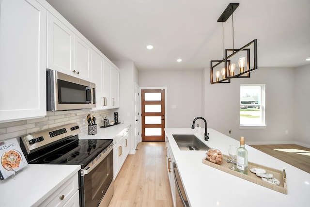 kitchen featuring a sink, stainless steel appliances, white cabinetry, tasteful backsplash, and light wood-type flooring