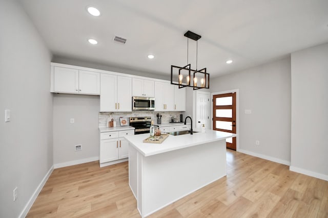 kitchen featuring light wood-type flooring, a sink, backsplash, appliances with stainless steel finishes, and light countertops