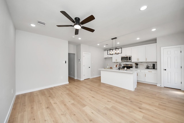 kitchen featuring visible vents, light wood finished floors, stainless steel appliances, decorative backsplash, and white cabinetry