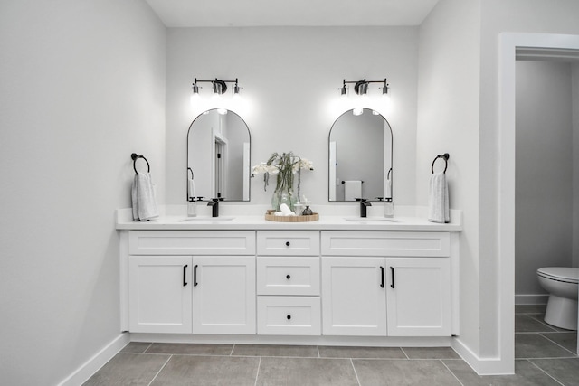 full bathroom featuring double vanity, toilet, baseboards, and a sink