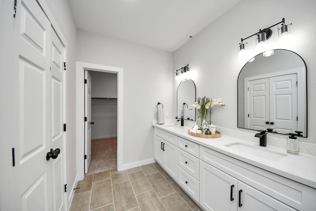 bathroom with a sink, a walk in closet, baseboards, and double vanity