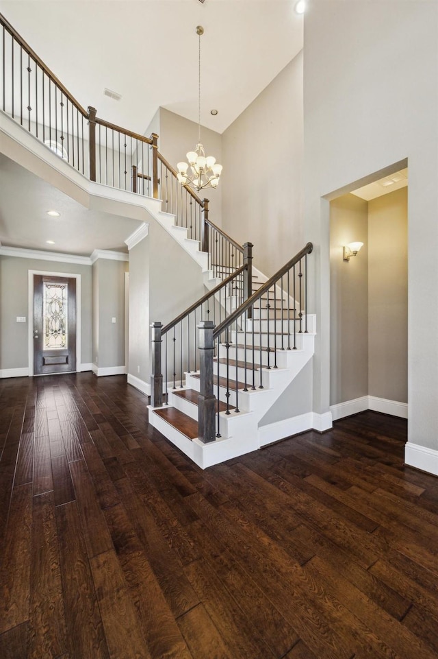 entrance foyer with hardwood / wood-style floors, stairway, a high ceiling, an inviting chandelier, and baseboards