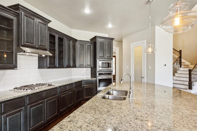 kitchen featuring backsplash, glass insert cabinets, under cabinet range hood, appliances with stainless steel finishes, and a sink