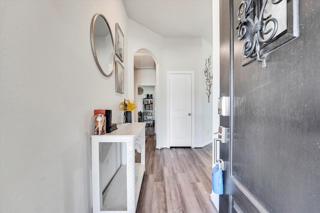 hallway with arched walkways, baseboards, and wood finished floors