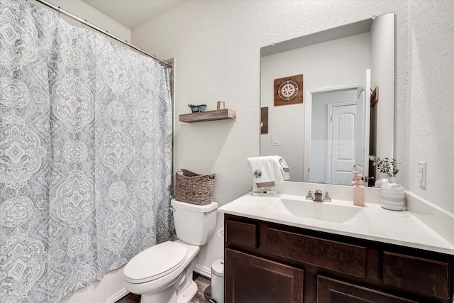 full bath with toilet, vanity, and a textured wall