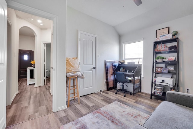 home office featuring baseboards, arched walkways, light wood-style floors, and lofted ceiling