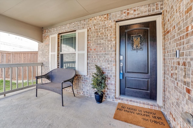 property entrance featuring a porch, fence, and brick siding