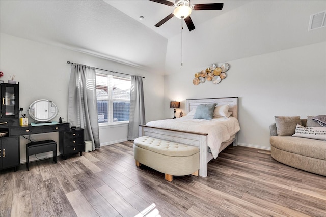 bedroom featuring a ceiling fan, wood finished floors, visible vents, baseboards, and vaulted ceiling