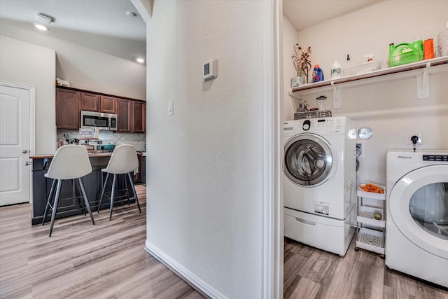 clothes washing area with laundry area, baseboards, light wood-type flooring, and washing machine and clothes dryer