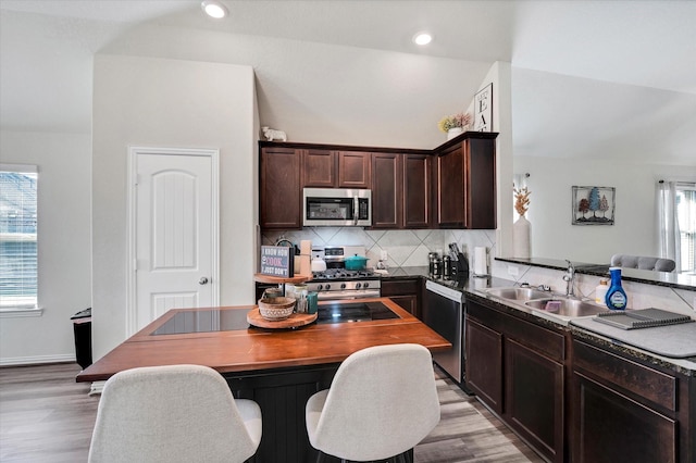 kitchen featuring a sink, appliances with stainless steel finishes, light wood finished floors, decorative backsplash, and dark brown cabinets