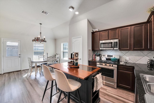 kitchen with visible vents, dark brown cabinets, a chandelier, vaulted ceiling, and stainless steel appliances