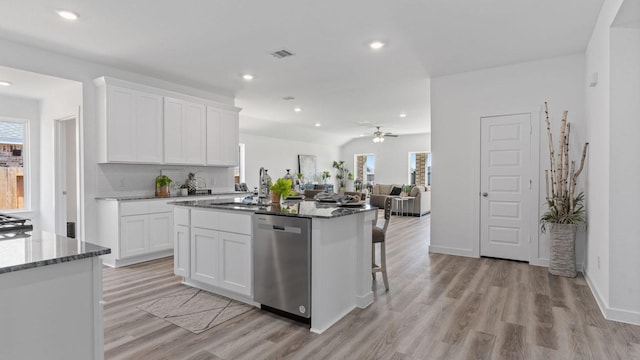 kitchen with visible vents, an island with sink, a sink, dark stone countertops, and dishwasher