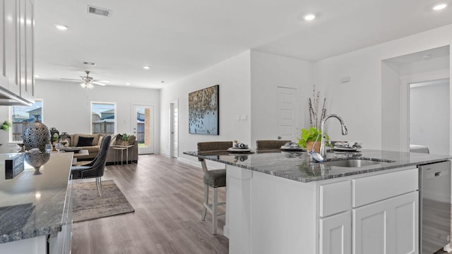 kitchen featuring visible vents, open floor plan, dishwasher, dark stone countertops, and a sink