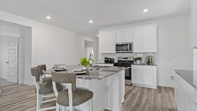 kitchen with a center island with sink, backsplash, stainless steel appliances, and light wood-style flooring