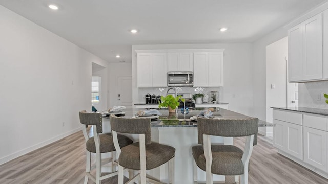 kitchen with light wood-style flooring, a breakfast bar area, white cabinets, and stainless steel appliances