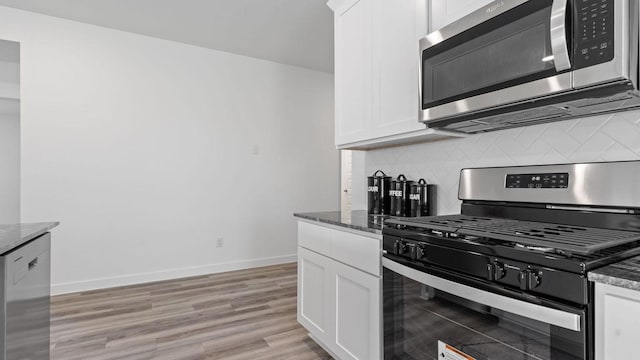 kitchen with decorative backsplash, dark stone countertops, white cabinetry, and stainless steel appliances