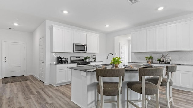 kitchen featuring a kitchen bar, a kitchen island with sink, a sink, light wood-style floors, and appliances with stainless steel finishes