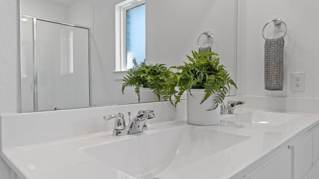 bathroom with a sink, a shower with shower door, and double vanity