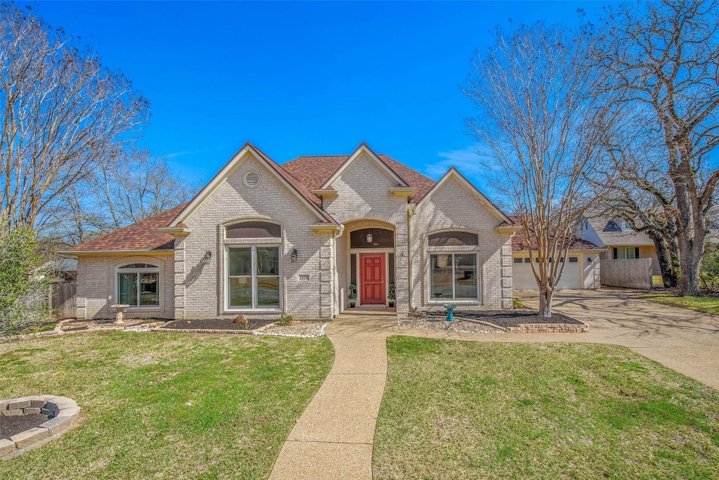 french country style house featuring brick siding, an attached garage, driveway, and a front lawn