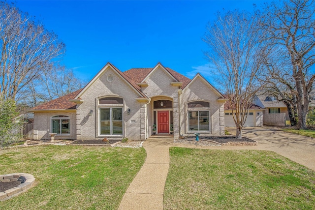 french country style house featuring brick siding, an attached garage, driveway, and a front lawn