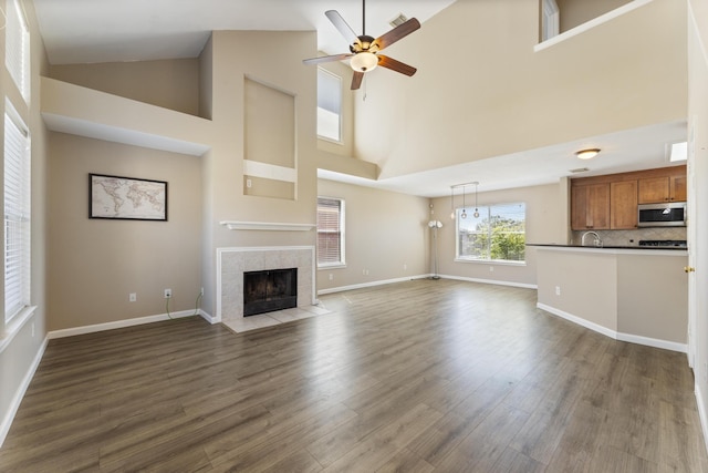 unfurnished living room with dark wood-type flooring, a fireplace, baseboards, and ceiling fan