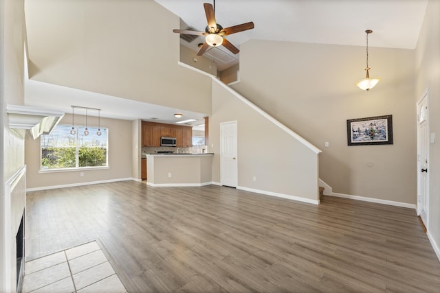 unfurnished living room with stairway, baseboards, ceiling fan, and wood finished floors